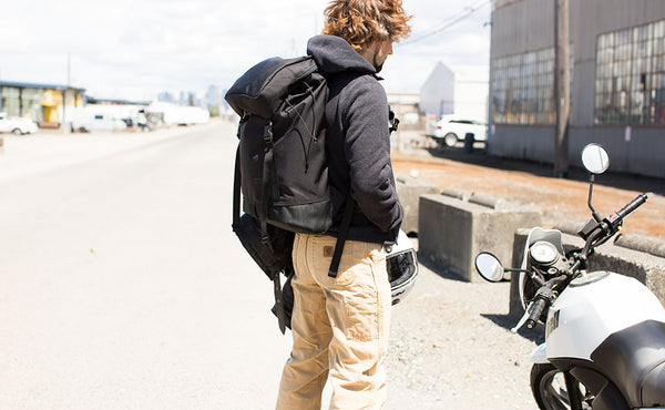 Nik wearing the Shadow Guide 33 while standing next to his Buell Blast motorcycle in the alley behind the TOM BIHN factory.